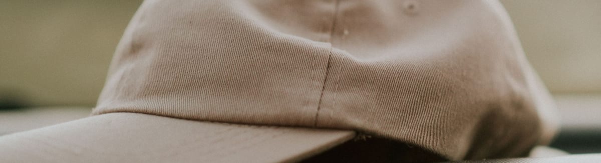 Plain tan cotton twill cap with an unstructured crown and a curved brim, showing the front panel a logo is stitched onto