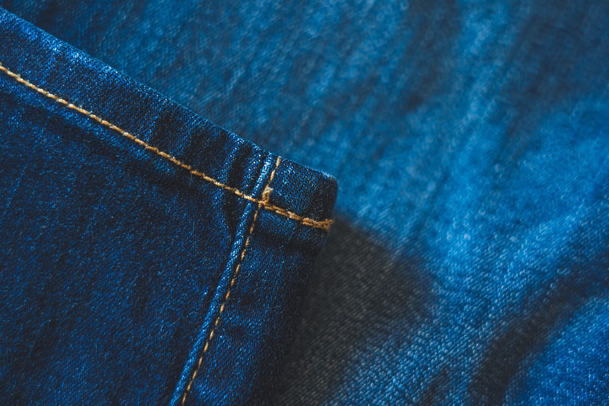 Close-up of a blue denim hem, showing the twill weave and the contrast stitching along two seams