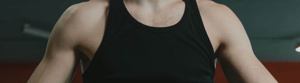 Black ribbed singlet worn in a dimly lit gym, with the shoulders, deep armholes and plain front panel in frame