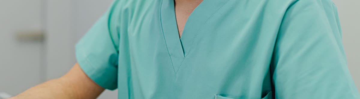 Teal V-neck scrub top with a chest pocket, worn in a bright clinical room