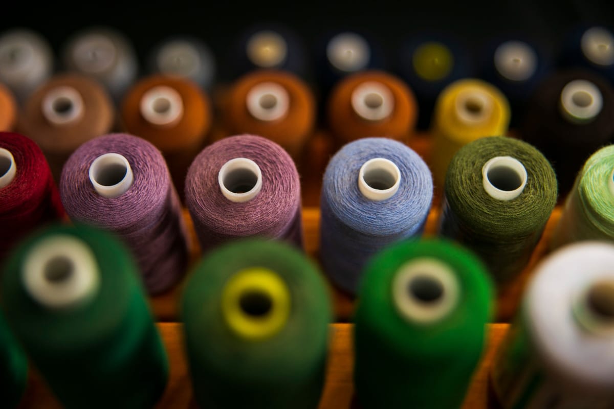 Cones of thread in a range of colours standing in a wooden rack, greens, purples, blues and oranges